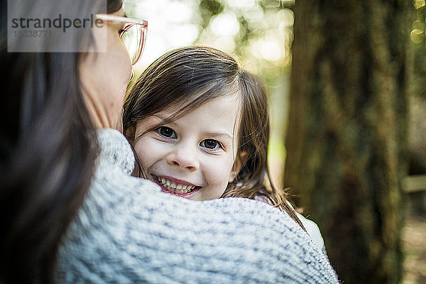 Hübsches junges Mädchen  das seiner Mutter im Wald über die Schulter schaut.