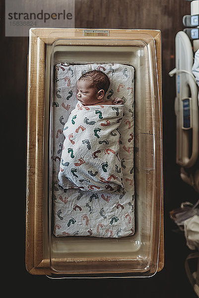 Draufsicht eines neugeborenen Jungen in Krankenhauswiege mit Decken