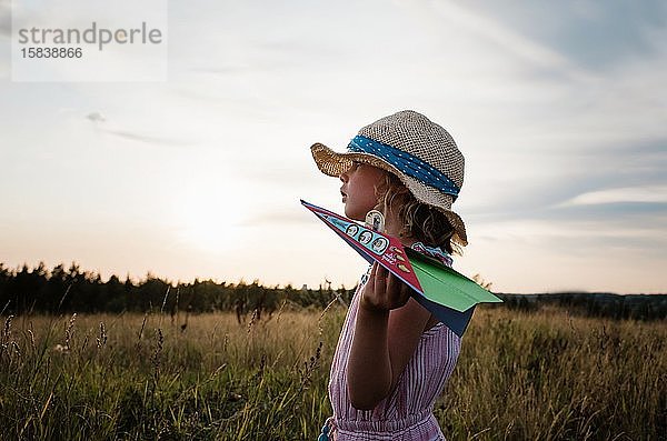 Profil eines Mädchens  das bei Sonnenuntergang auf einer Wiese mit Papierflugzeugen spielt