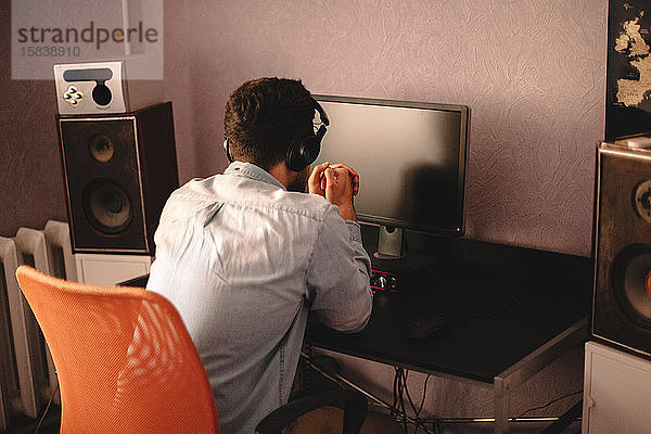 Konzentrierter Mann mit Kopfhörern am Desktop-Computer sitzend