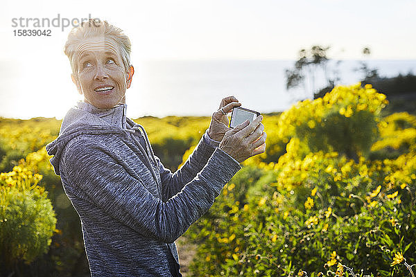 Ältere Frau schaut weg  während sie durch ein Smartphone gegen den Himmel fotografiert