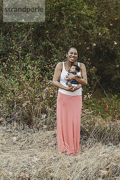 Porträt einer jungen Mutter  die eine Tochter im neugeborenen Alter im Freien hält