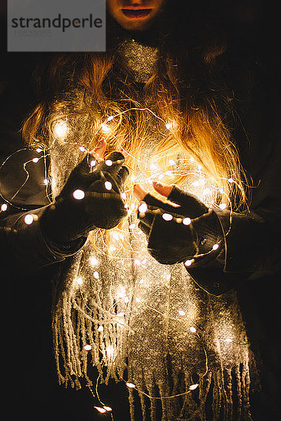Junge Frau hält Weihnachtsbeleuchtung im Dunkeln im Freien