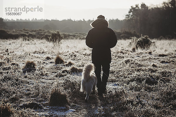 Rückansicht eines Mannes  der an einem kalten  frostigen Morgen mit seinem Hund über die Heide spaziert