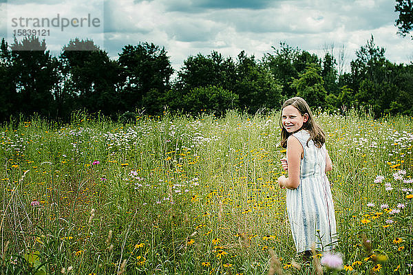 Lächelndes Mädchen schaut über die Schulter in einem Feld voller Wildblumen