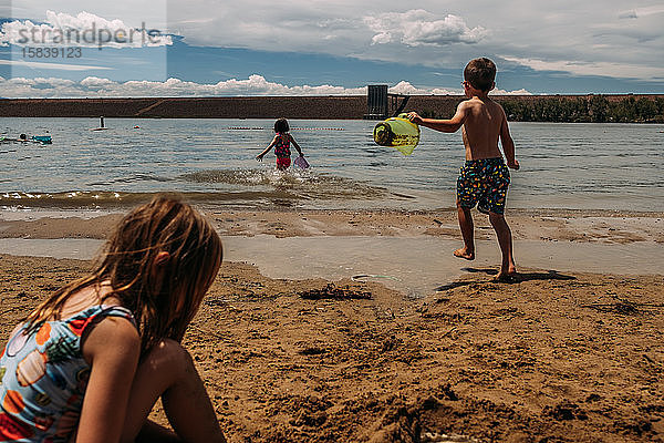 kleine Kinder  die im Sommer im Sand an einem See spielen