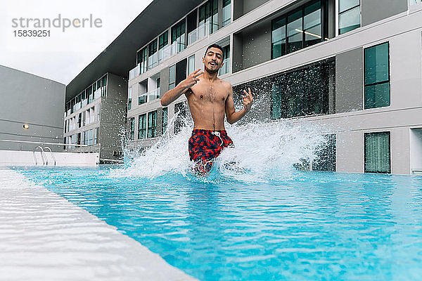 Junger Mann springt in einen von Gebäuden umgebenen Pool