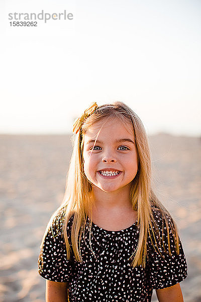 Junges Mädchen lächelt vor der Kamera am Strand bei Sonnenuntergang