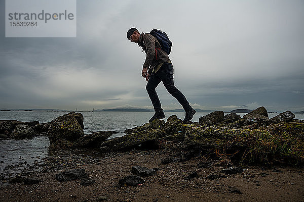 Wanderer geht über moosbewachsene Schlammsteine vom Bauwerk am Strand der Bucht