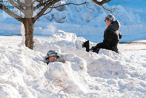 Zwei Jungen bauen an einem sonnigen Wintertag mit Schaufeln Schneefestungen.