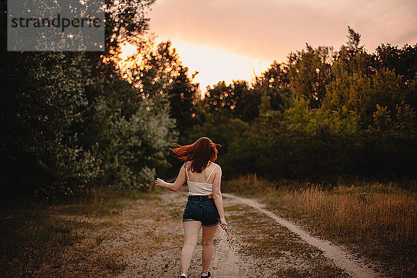 Rückansicht einer jungen Frau  die im Sommer auf einem Waldweg geht