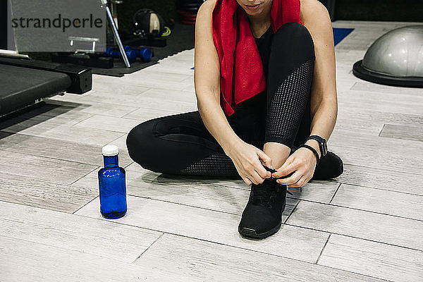 junge Frau  die ihre Schnürsenkel im Fitnessstudio bindet