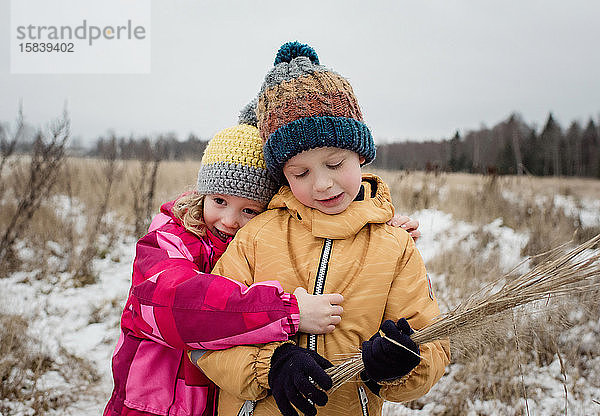 Geschwister kuscheln beim Spielen draussen im Schnee