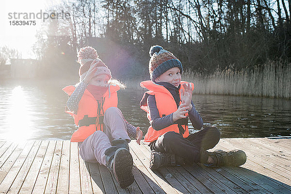 Bruder und Schwester spielen im Winter lachend auf einem Steg am Strand