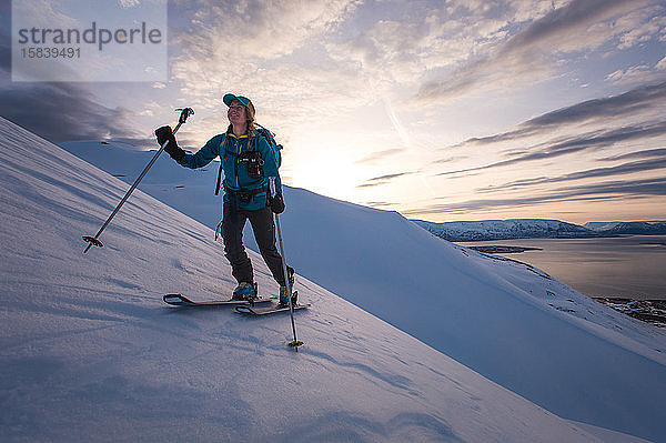 Frau beim Skilanglauf in Island bei Sonnenaufgang mit Wasser im Rücken