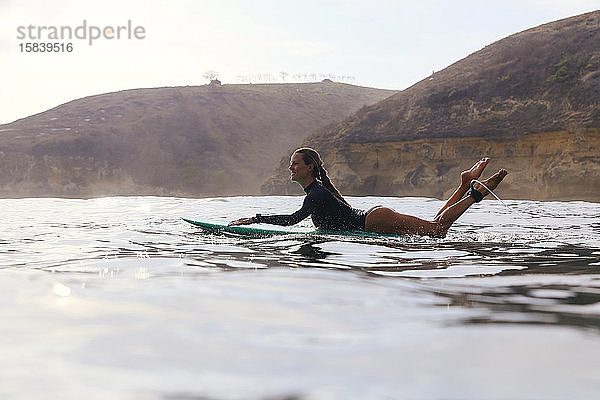 Glückliche Frau sitzt auf einem Surfbrett im Meer