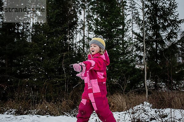 Mädchen spielt im Schnee lachend und wirft einen Schneeball