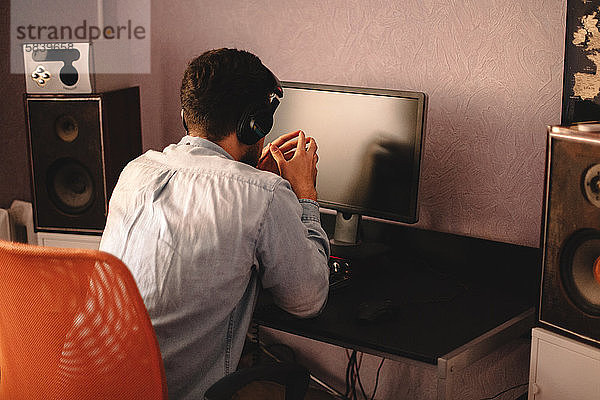 Konzentrierter Mann hört Musik über Kopfhörer am Computer sitzend