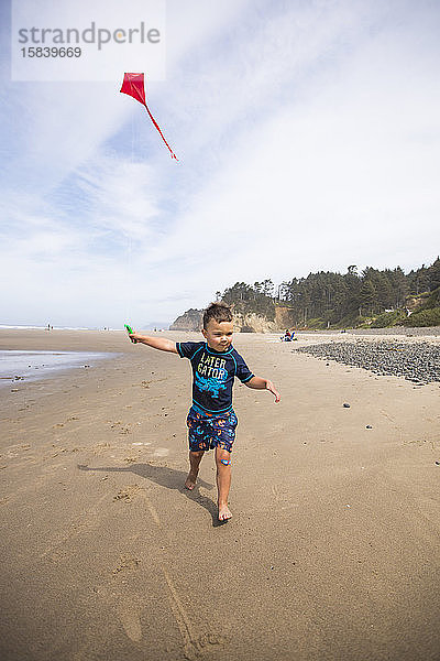 Junge läuft mit einem Drachen am Strand von Oregon Coast.