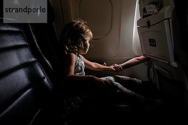 kleines Mädchen im Flugzeug  das mit seiner Schwester in einem anderen Gang Händchen hält