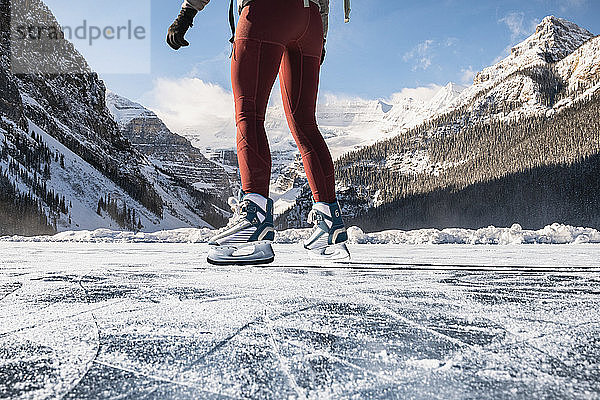 Junge Frau läuft an einem kalten Wintertag auf dem gefrorenen Lake Louise Schlittschuh