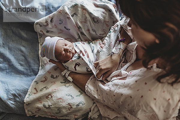 Draufsicht auf die Mutter  die den neugeborenen Jungen mit Hut im Krankenhausbett hält