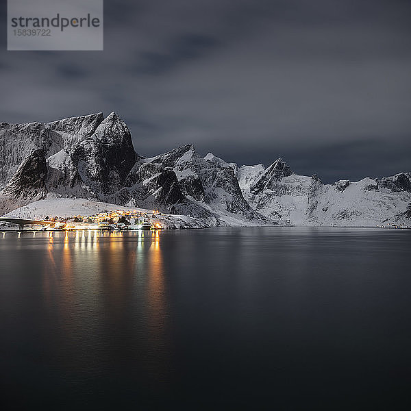 Dorflichter leuchten in einer mondhellen Winternacht in der Nähe von Reine  MoskenesÃ¸y  Lofoten Inseln  Norwegen