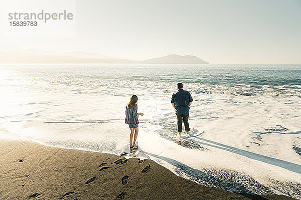 Vater und Tochter gehen bei Sonnenuntergang am Strand im Wasser