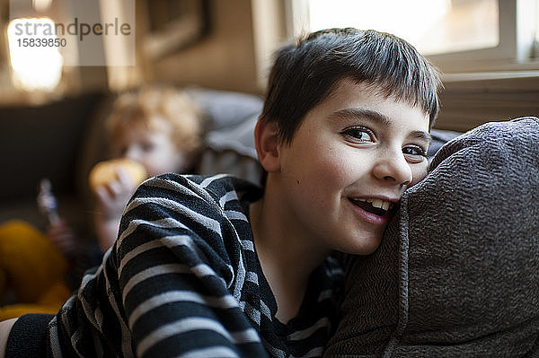 Glücklicher 7-8-jähriger Junge liegt lächelnd zu Hause auf der Couch
