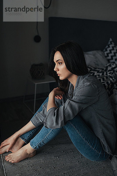Eine junge einsame Frau sitzt auf dem Boden in einem dunklen Raum