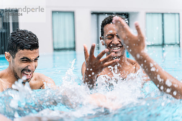 Mann lächelt  während er im Kreis mit einer Gruppe von Freunden in einem Pool spielt