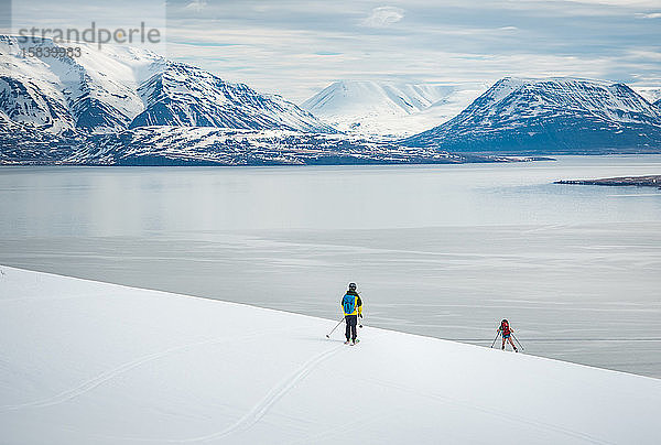 Zwei Menschen fahren in Island auf Skiern Richtung Meer