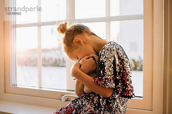 ein junges Mädchen  das zu Hause in einem funkelnden Kleid bei Sonnenuntergang mit seinem Spielzeug spielt