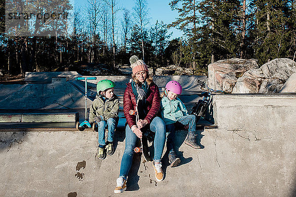 Mama sitzt mit ihren Kindern auf einem Skatepark im Freien und amüsiert sich
