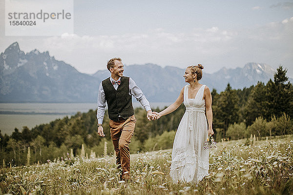 glückliche Braut und Bräutigam gehen durchs Feld vor den Bergen Wyoming