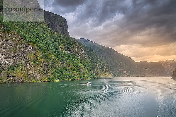 Kleines Boot fährt bei Sonnenuntergang in den erstaunlichen Fjorden Norwegens