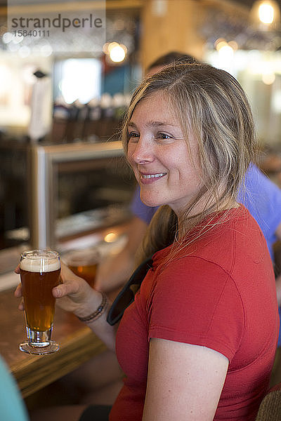 Eine junge Frau genießt ein Bier mit ihren Freunden in einer Bar in Oregon.