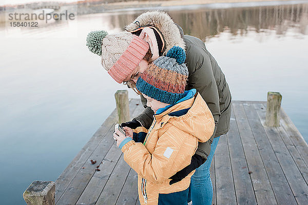 Mutter  die sich Bilder einer Kamera ansieht  während ihr Sohn im Winter draußen ist
