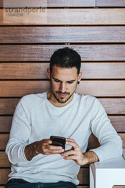 Porträt eines jungen Mannes  der mit seinem Handy in einem Café sitzt