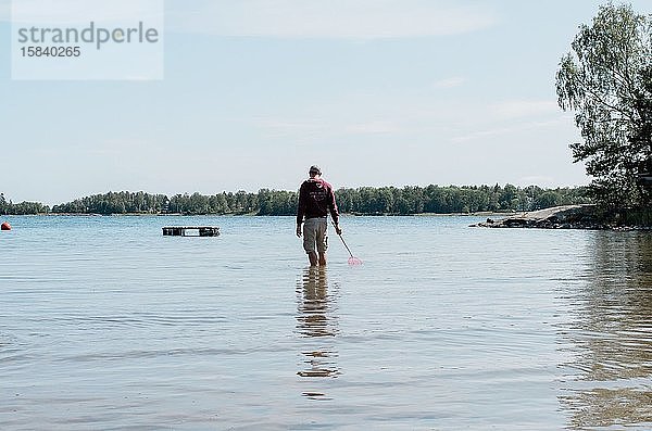 Mann  der im Sommer mit einem Fischernetz im Wasser steht