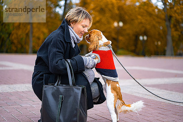 Frau bei einem Spaziergang im Park mit einem Hund von Cavalier King Charles Spaniel.