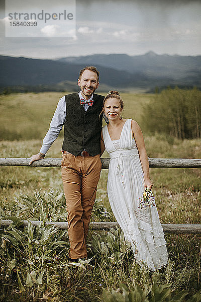 Lächelndes glückliches Brautpaar lehnt an Zaun auf Feld in Wyoming