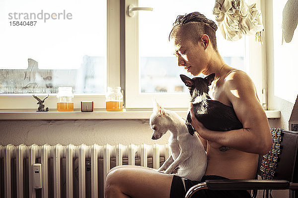 schöne starke Frau sitzt im warmen Fensterlicht mit zwei kleinen Hunden