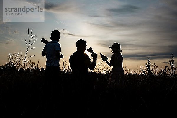 Silhouette eines Vaters  der mit Sohn und Tochter bei Sonnenuntergang draußen spielt