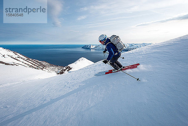 Ein Mann auf Skiern mit Ozean im Hintergrund in Island