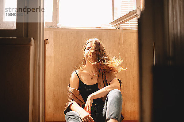 Junge Frau wirft Haare  während sie zu Hause auf dem Boden auf dem Balkon sitzt