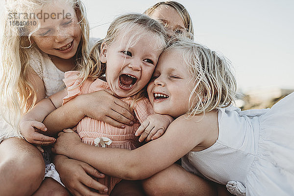 Nahaufnahme eines lachenden Kleinkindes umgeben von jungen Schwestern