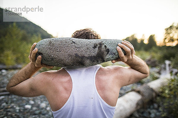 Rückansicht eines Mannes  der einen großen Felsen als Teil eines Trainings im Freien benutzt.
