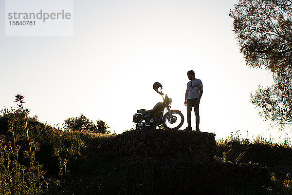 Hintergrundbeleuchtung eines Mannes  der sein schönes Motorrad auf einem Felsen in der