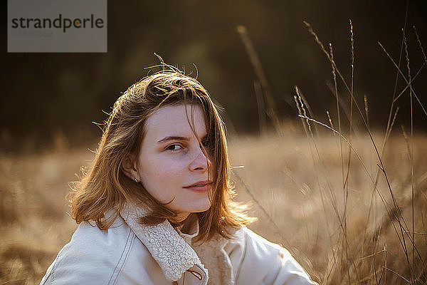 Schöne Frau sitzt bei Sonnenuntergang auf weichem  trockenem Gras.